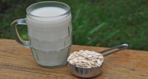 A mug of oat milk next to a small metal measuring cup brimming with oats, sitting on a wooden railing outside. Credit: Lincoln Zotarelli, UF/IFAS